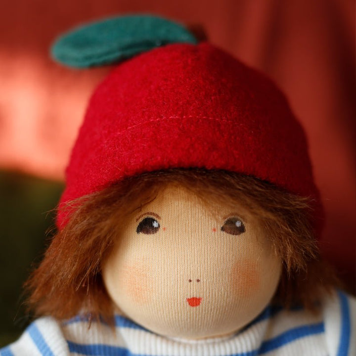 Detailaufnahme vom Gesicht von Gartenkind Loki – handbemalte braune Augen, Mohair‑Haare und rotes Blatt‑Häubchen